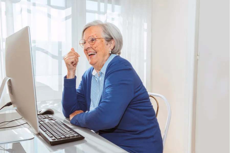 Senior woman smiling while using a computer in a bright independent living apartment in Clearwater